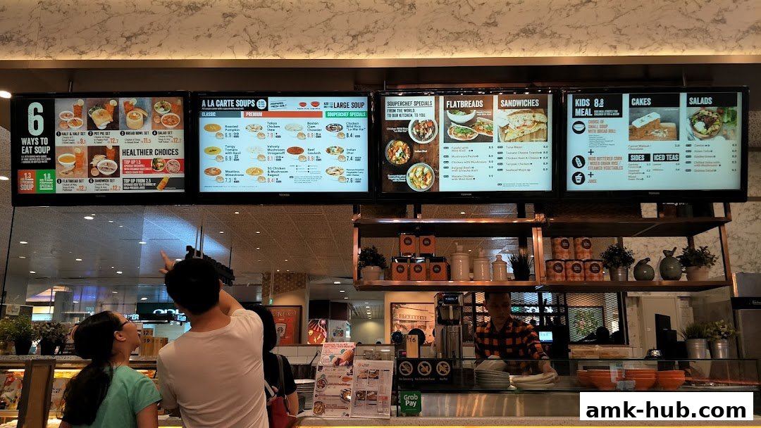 Digital menu boards displaying various soup sets, flatbreads, sandwiches, kids meals, cakes, and salads.
