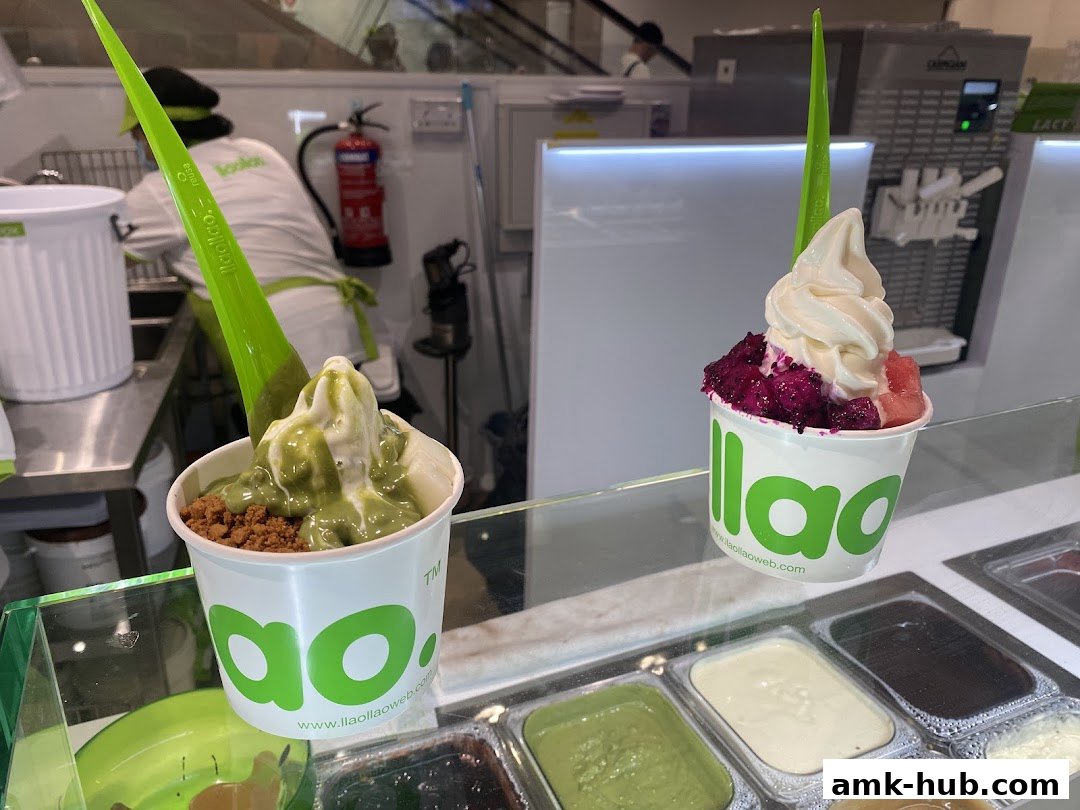 Two cups of frozen yogurt with toppings and a display of yogurt flavors.