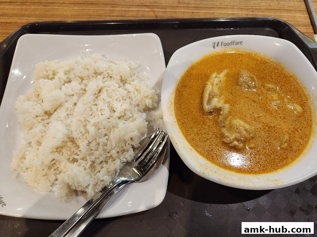 A bowl of curry with chicken and a side of white rice, served with cutlery.