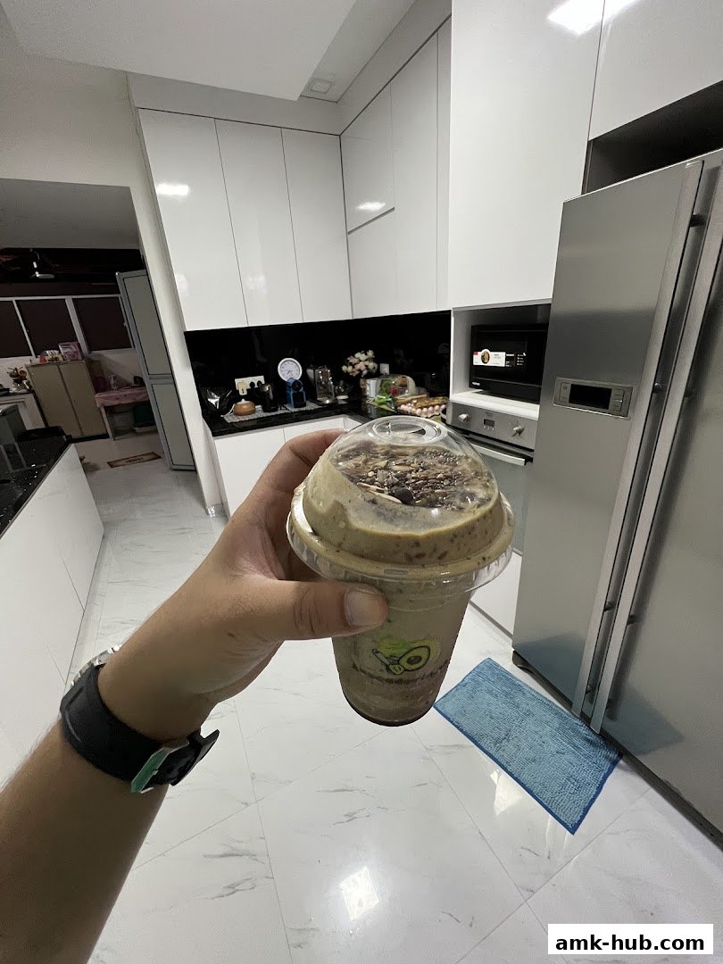 A hand holds a blended avocado drink with toppings in a modern kitchen.