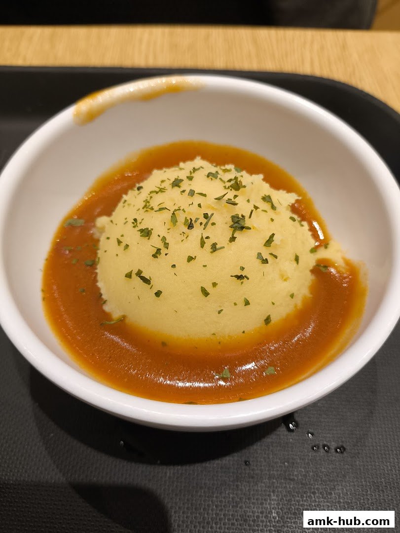 A close-up shot of mashed potatoes topped with herbs and surrounded by a savory sauce.