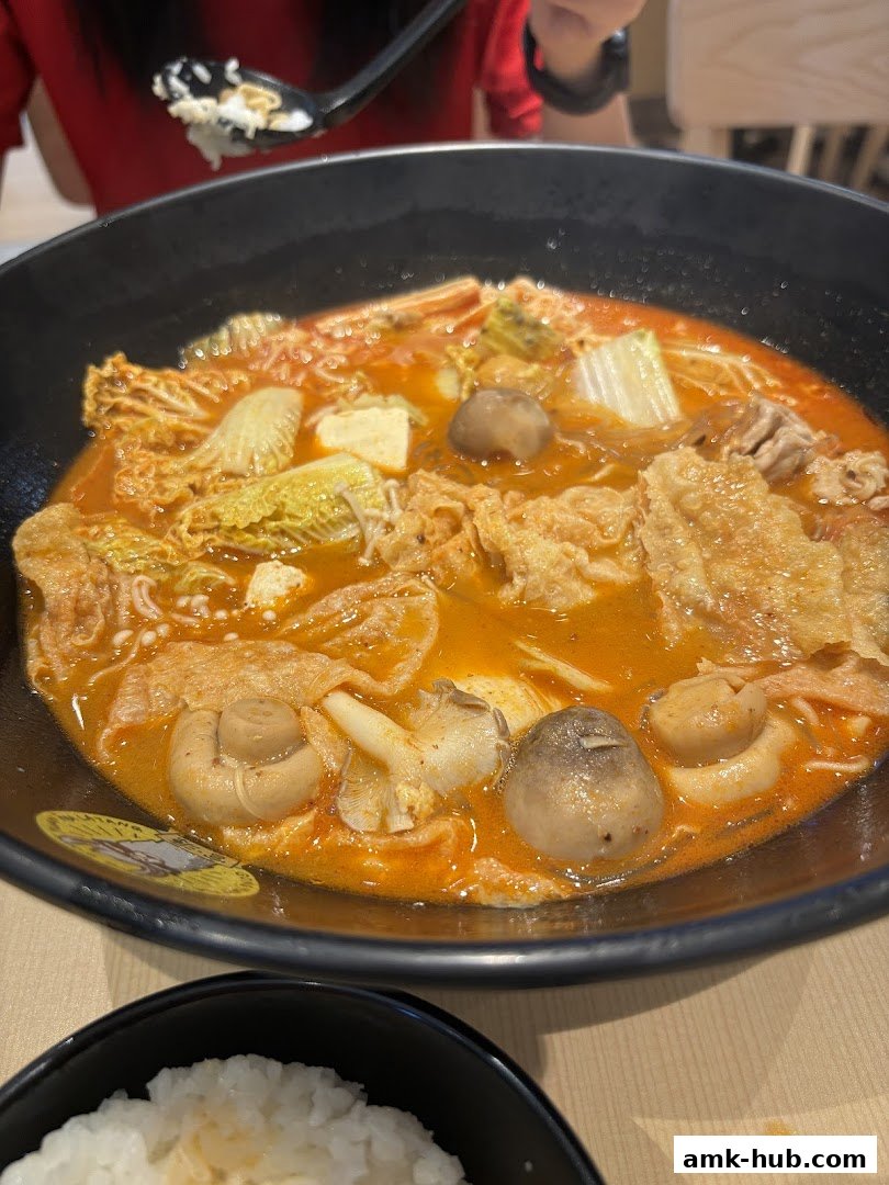 A close-up of a steaming bowl of Mala Tang with various ingredients and a side of rice.