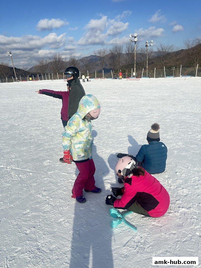 Children in ski gear on a snowy slope with mountains in the background.
