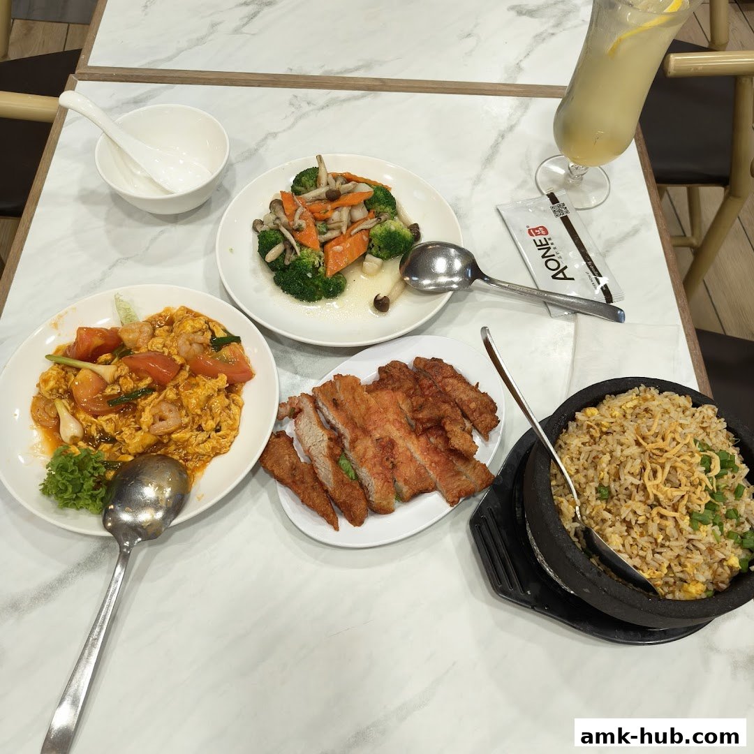 A table laden with various dishes including fried pork, stir-fried vegetables, fried rice, and a drink.