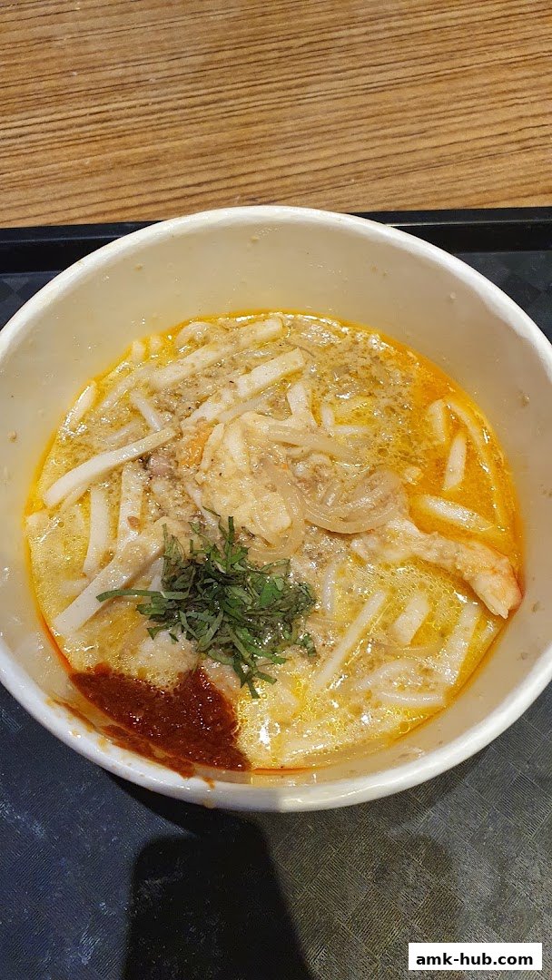 A close-up shot of a delicious bowl of Laksa with noodles, shrimp, and chili paste.