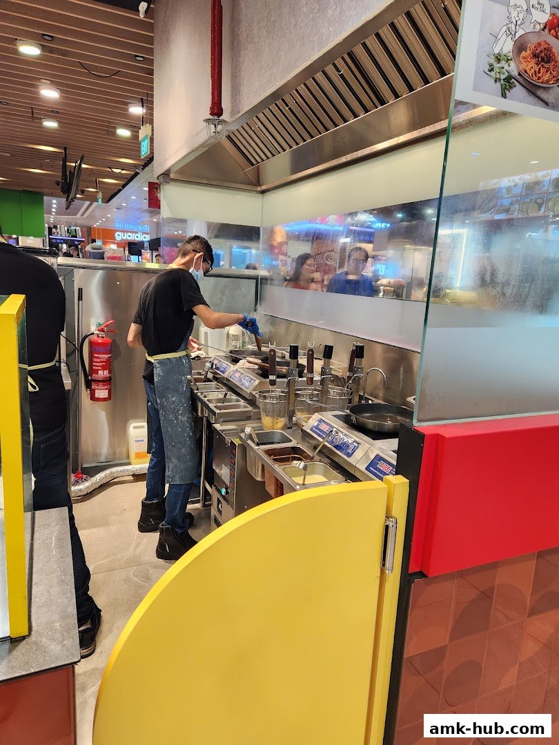 Staff preparing pasta dishes in a modern, open kitchen with stainless steel equipment.