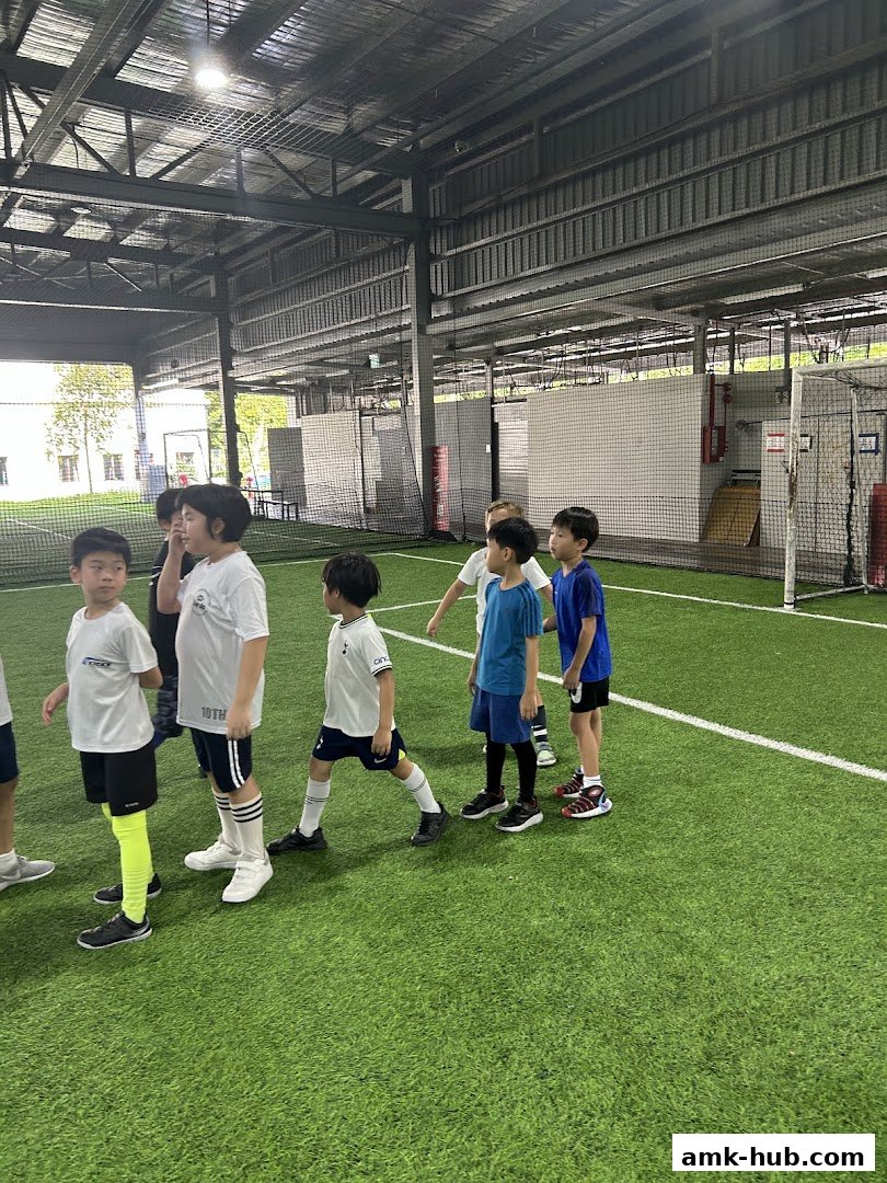 Children in sportswear gathered on an indoor artificial turf field.