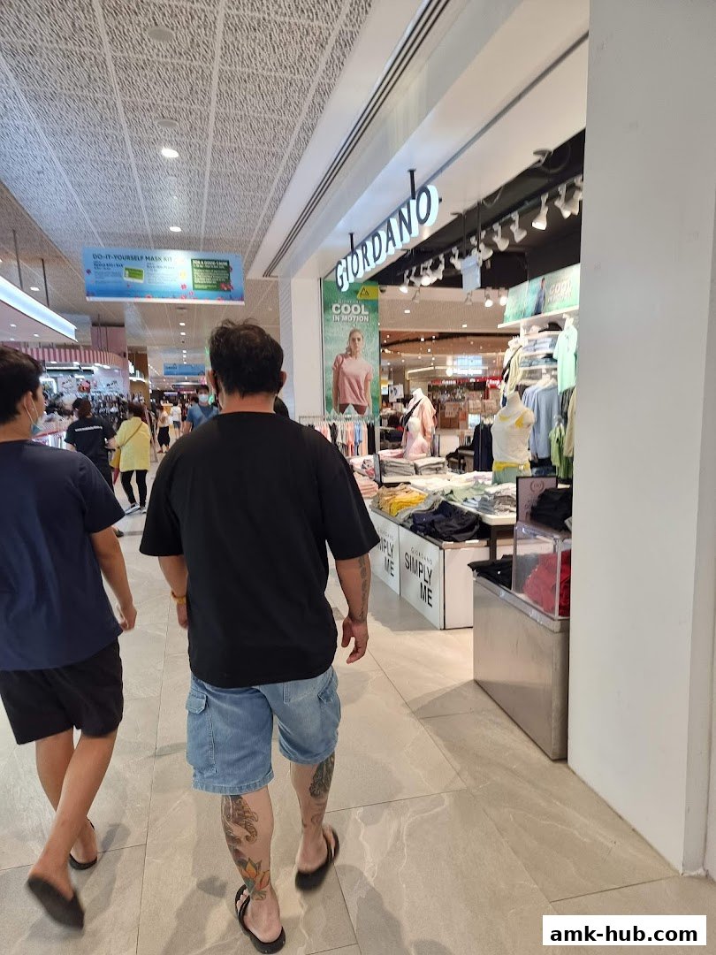 People walking past a Giordano clothing store entrance with displays of apparel.