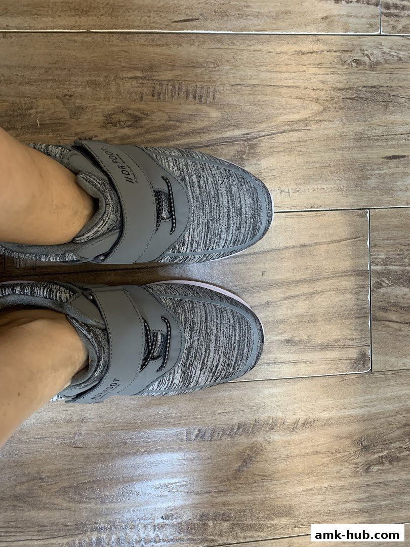A person's feet wearing comfortable grey and white speckled shoes with velcro straps.