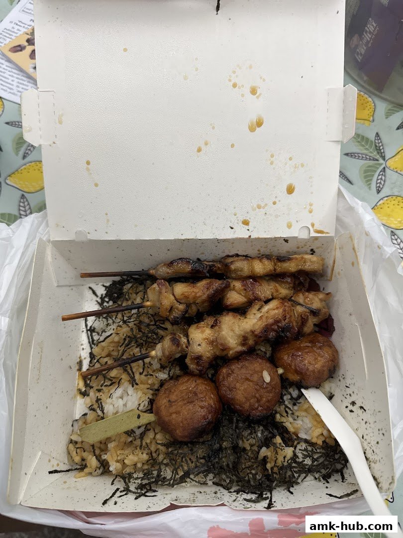 A takeout box filled with grilled chicken skewers, rice, and seaweed.