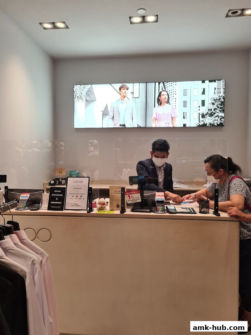 Two people at a checkout counter in a clothing store, with a digital display above.