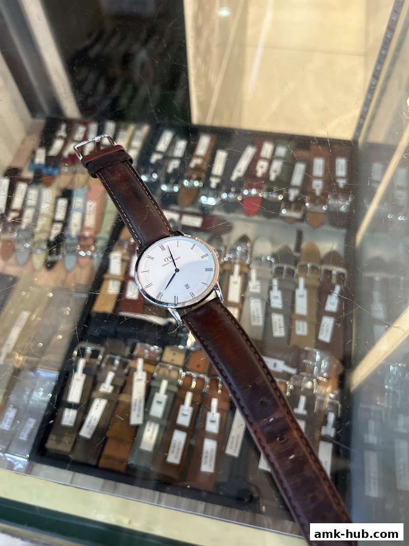 A close-up of a classic watch with a brown leather strap displayed in a shop window.