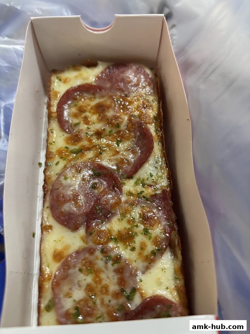 A close-up shot of a rectangular slice of pepperoni pizza in a white cardboard box.