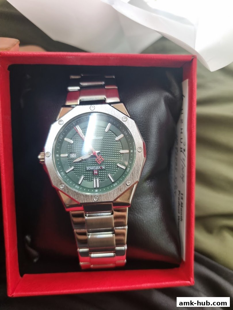 A stylish silver watch with a green dial is presented in a red gift box.