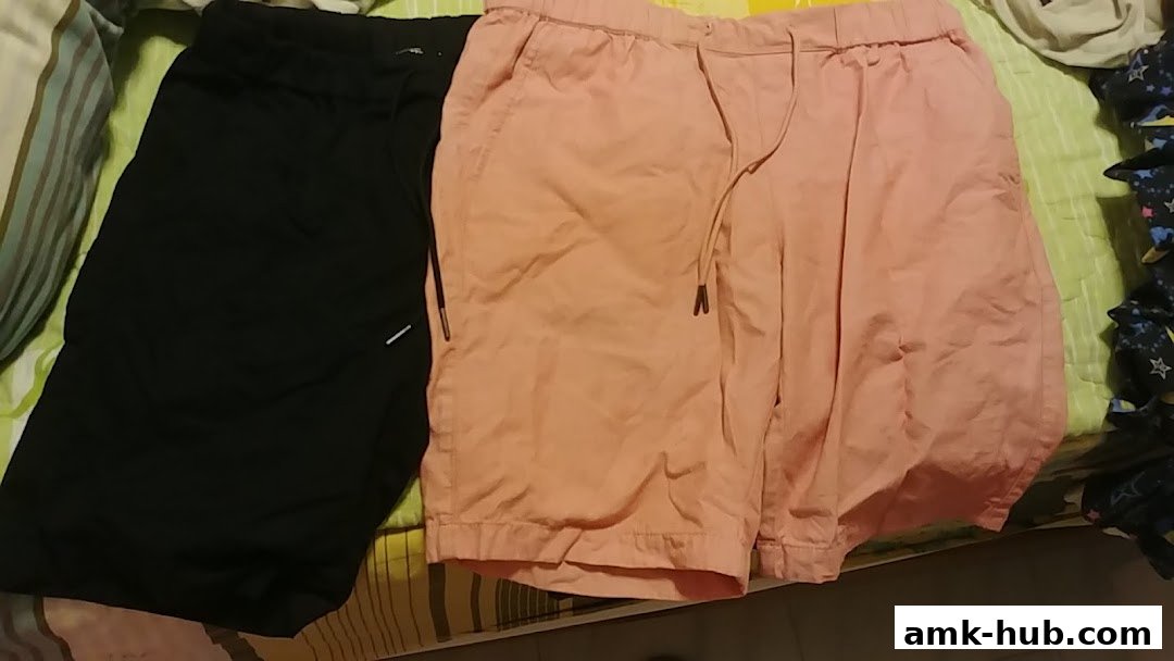 Two pairs of casual shorts, one black and one peach, laid out on a striped surface.