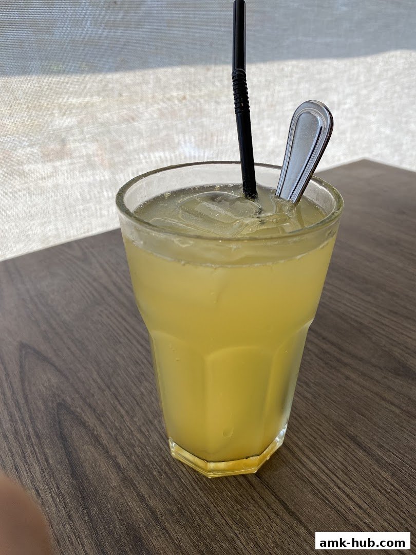 A refreshing yellow beverage with ice, a straw, and a spoon in a glass on a wooden table.