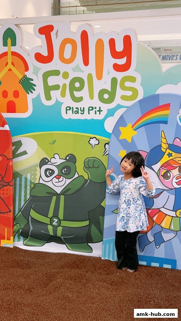 A young girl poses in front of a colorful play pit backdrop featuring cartoon characters.
