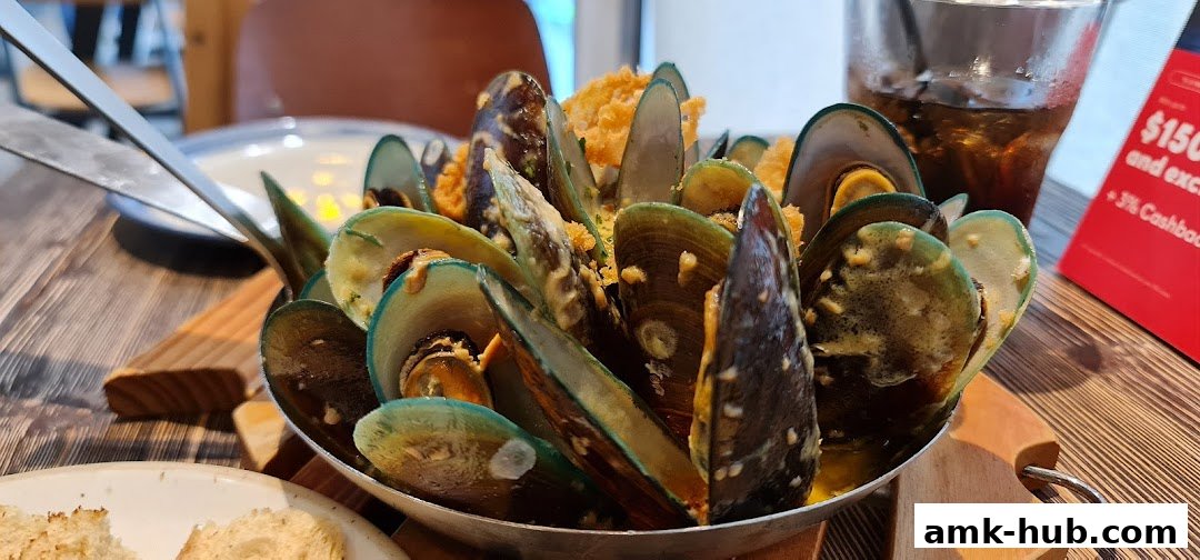 A close-up of a steaming bowl of mussels served with bread and a drink.