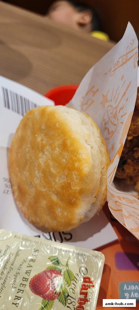 A close-up of a golden-brown biscuit with a packet of strawberry fruit spread.