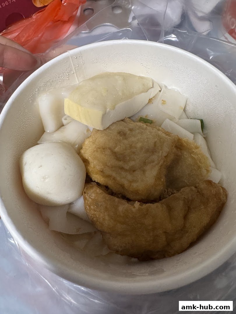 A bowl of Koo Kee noodles with fish balls, tofu, and fried items.