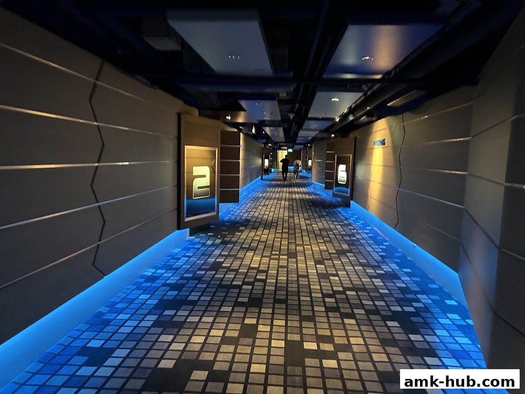A modern cinema hallway with illuminated room numbers and a patterned carpet.