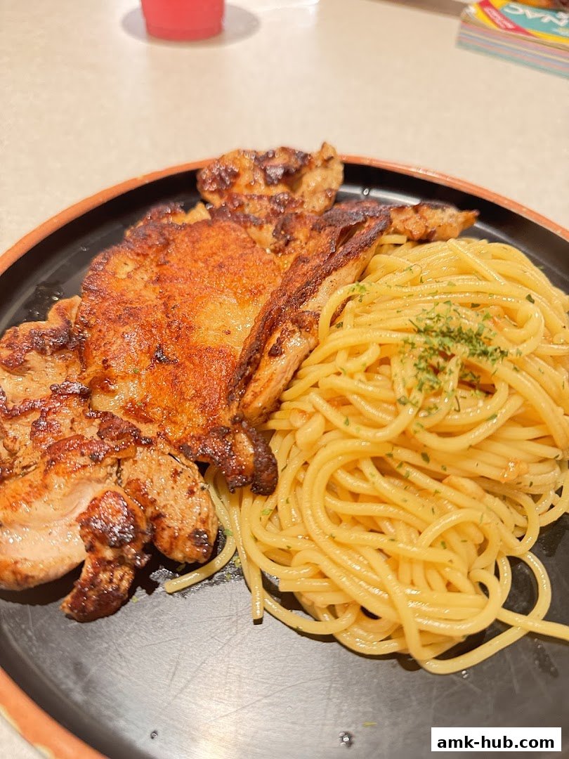 A close-up shot of a grilled chicken chop served with spaghetti on a black plate.