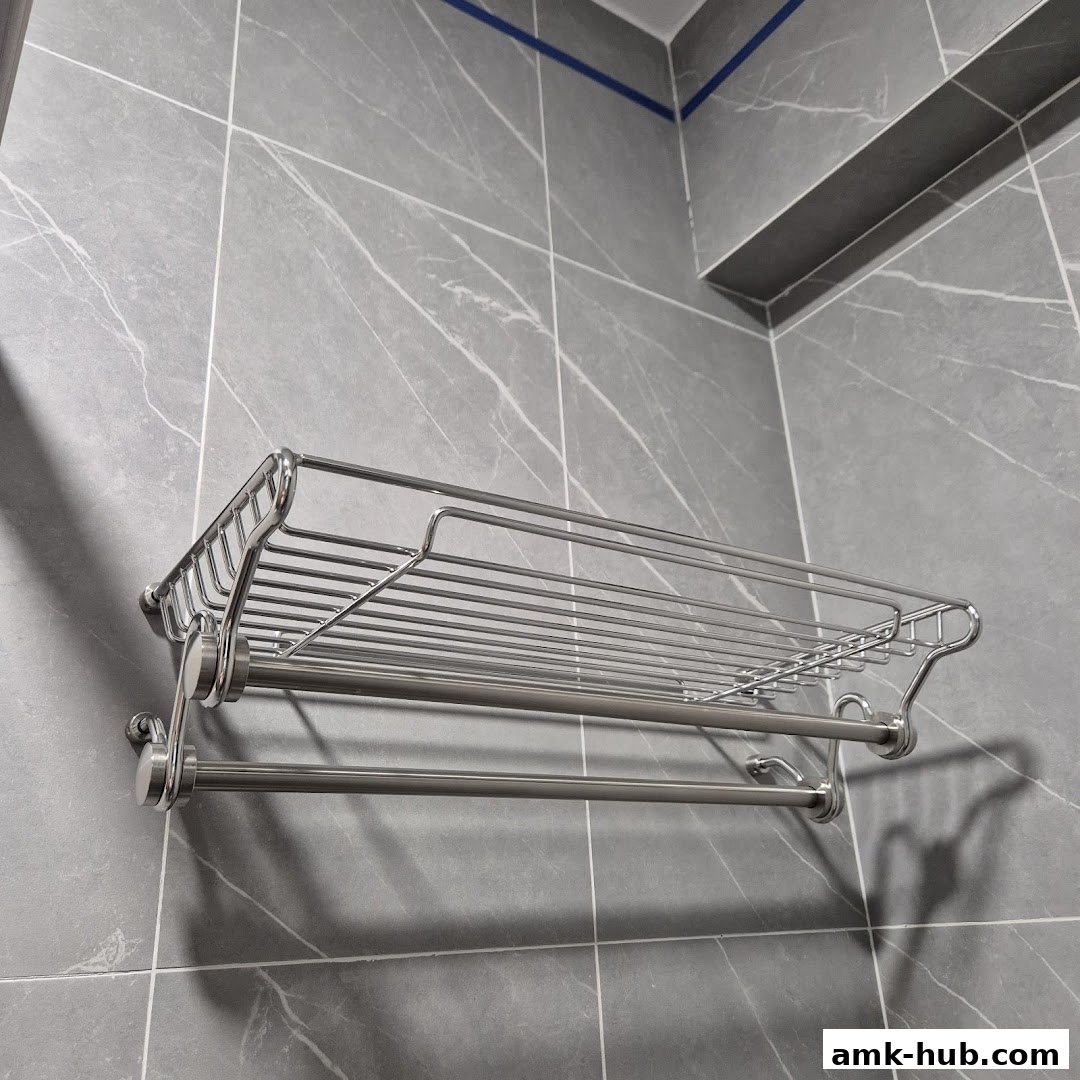 A stainless steel bathroom shelf with a towel bar mounted on a grey tiled wall.