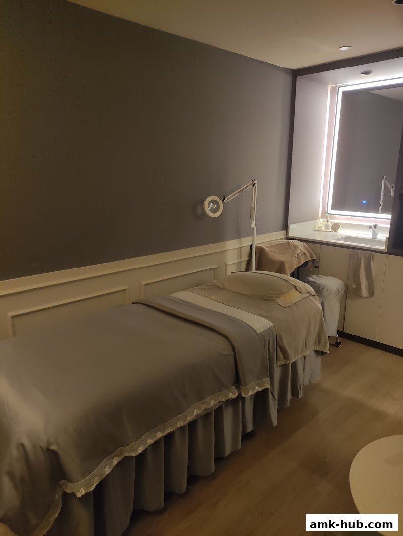 A treatment room with a massage bed, lamp, and a vanity with a mirror.
