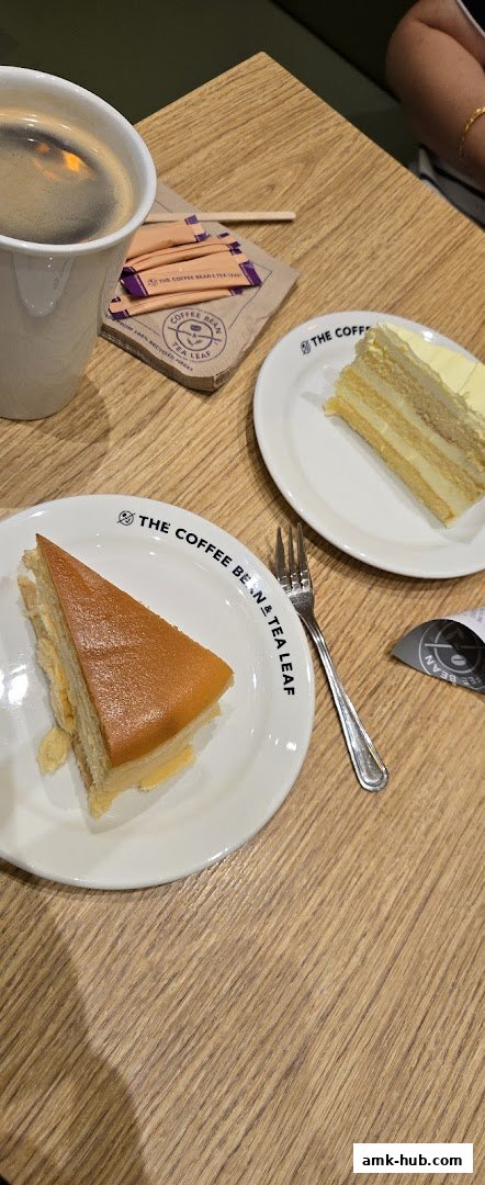 A close-up shot of two slices of cake and a cup of coffee on a wooden table.