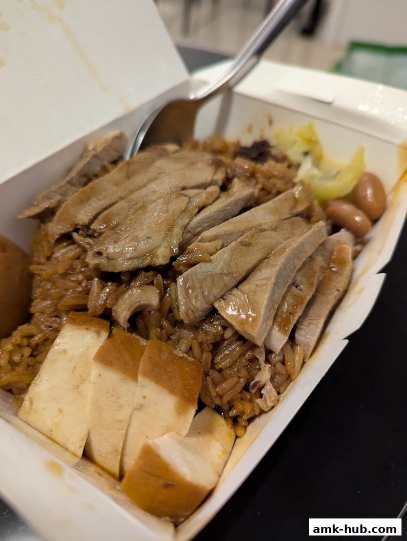 A close-up of a takeaway box filled with rice, sliced meat, tofu, and peanuts.