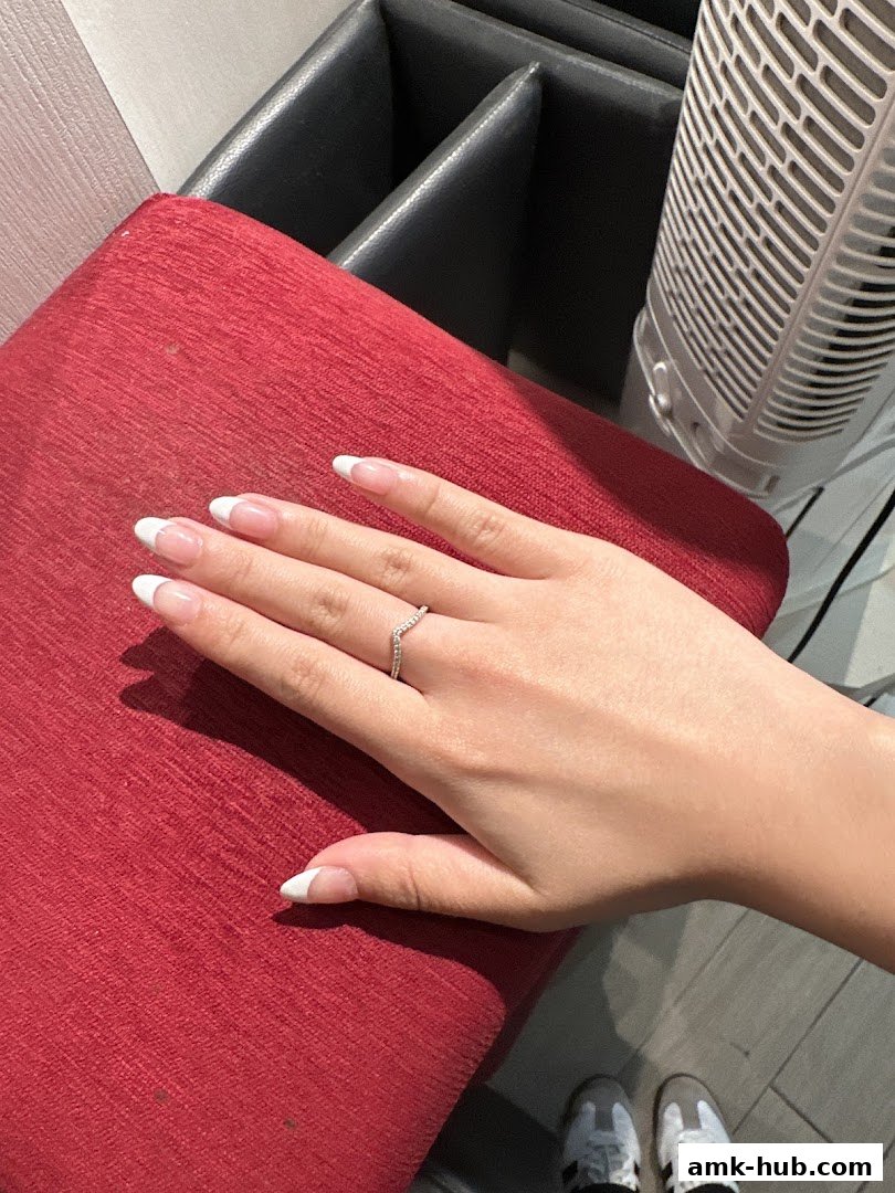 A hand with a French manicure and a ring rests on a red textured surface.