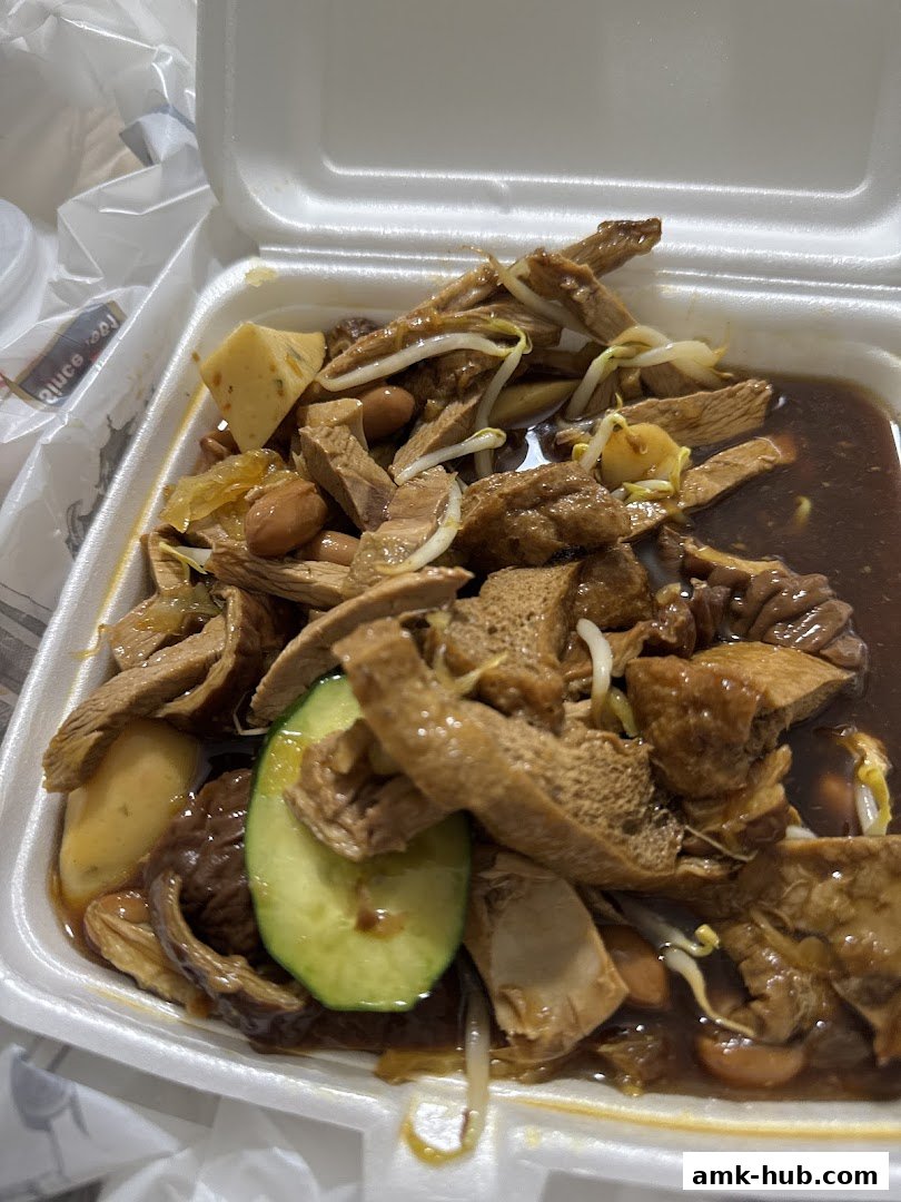 A close-up of a take-out container filled with braised ingredients and bean sprouts.