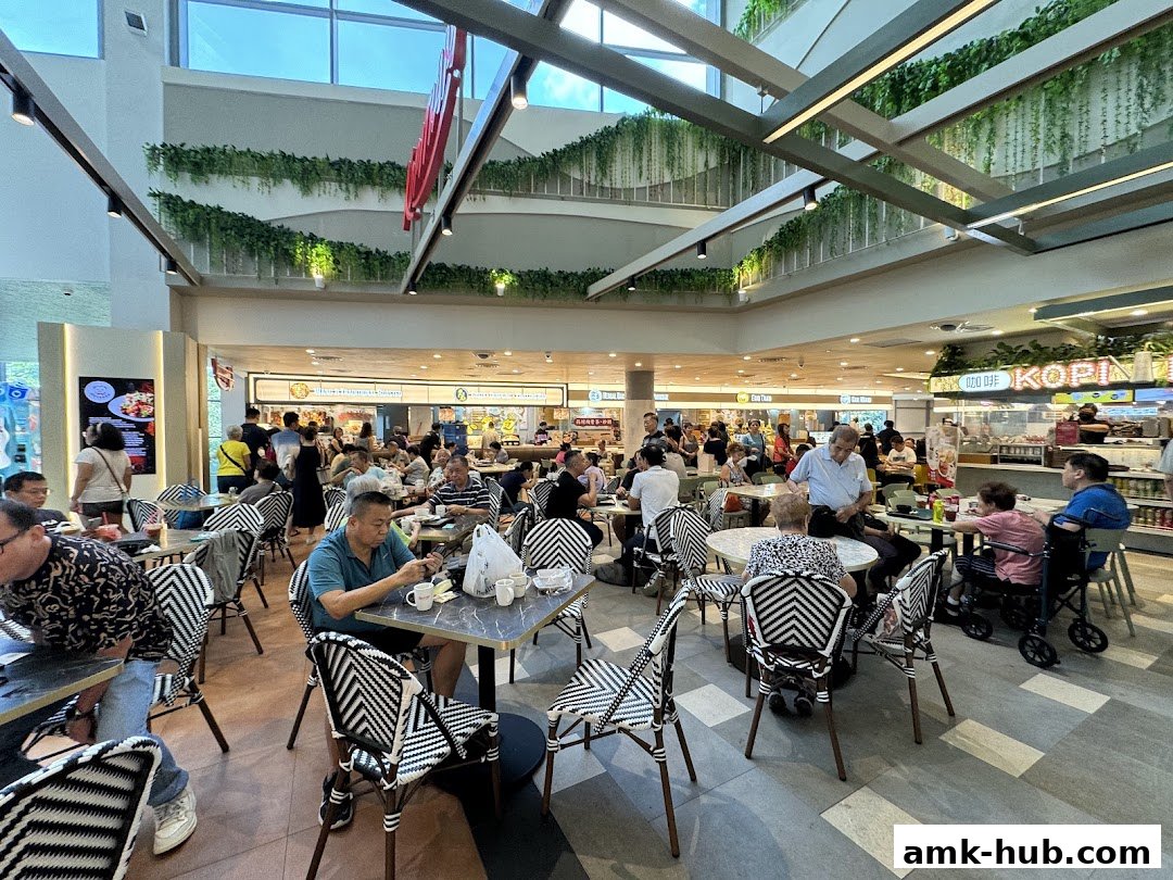 A busy food court with many people dining at tables, featuring a Kopitiam stall.