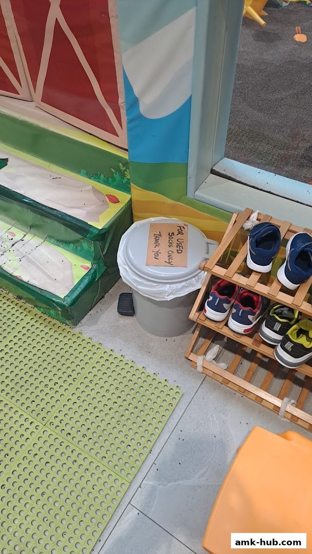 A shoe rack with children's shoes next to a trash can with a sign.