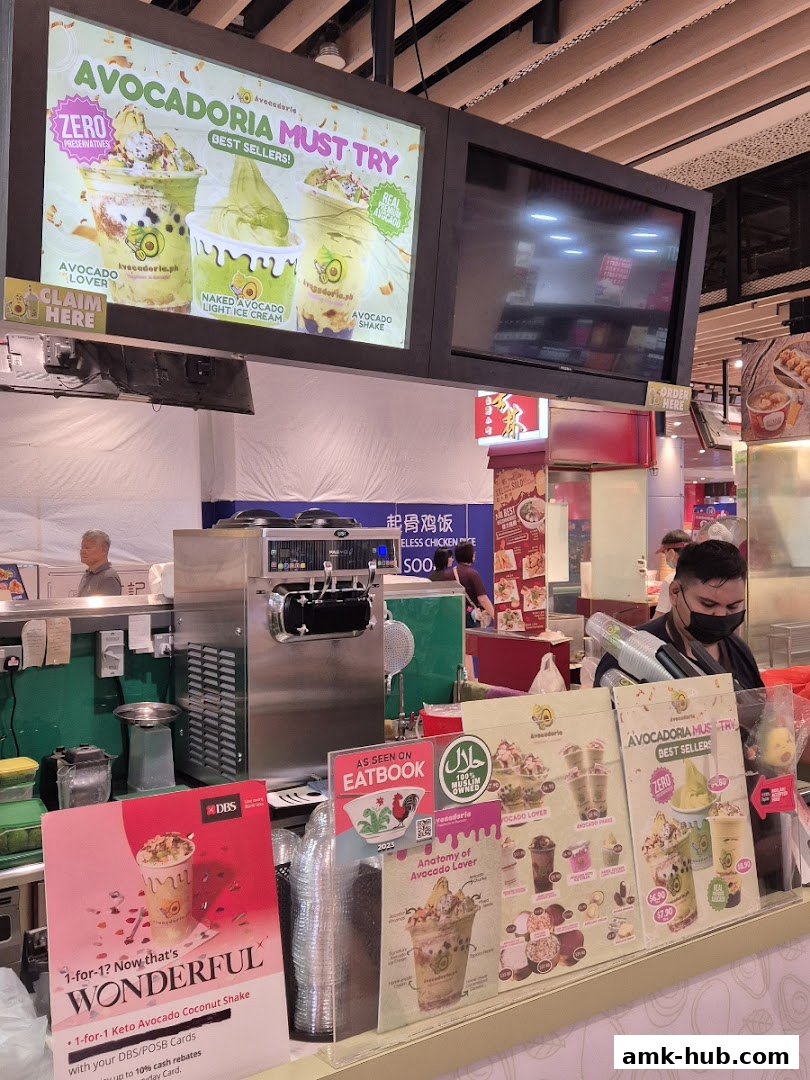 A food stall counter displaying avocado-based desserts and drinks, with a soft-serve machine in the background.
