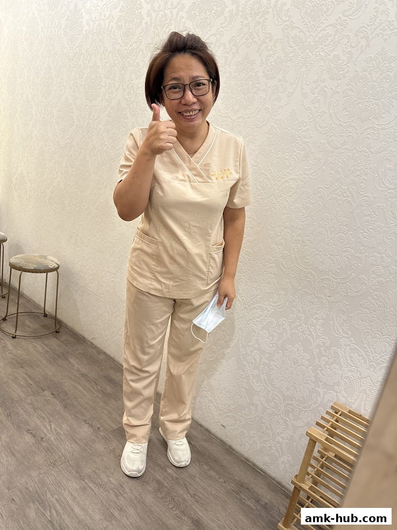 A smiling woman in a beige uniform gives a thumbs-up, holding a mask.