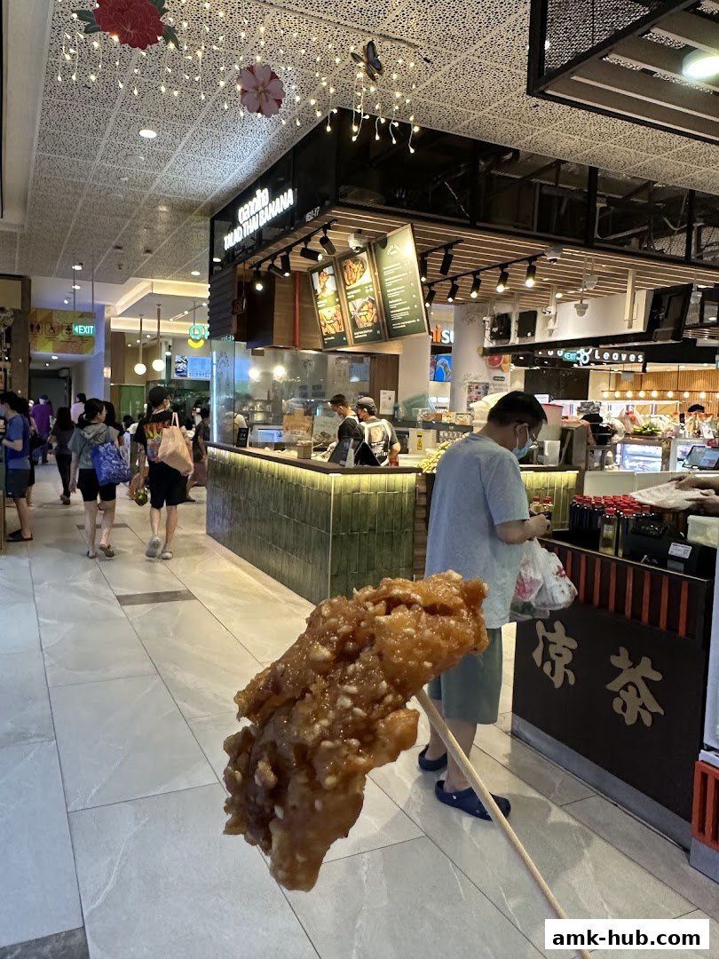 A person holds a skewer of fried food in front of a food stall.