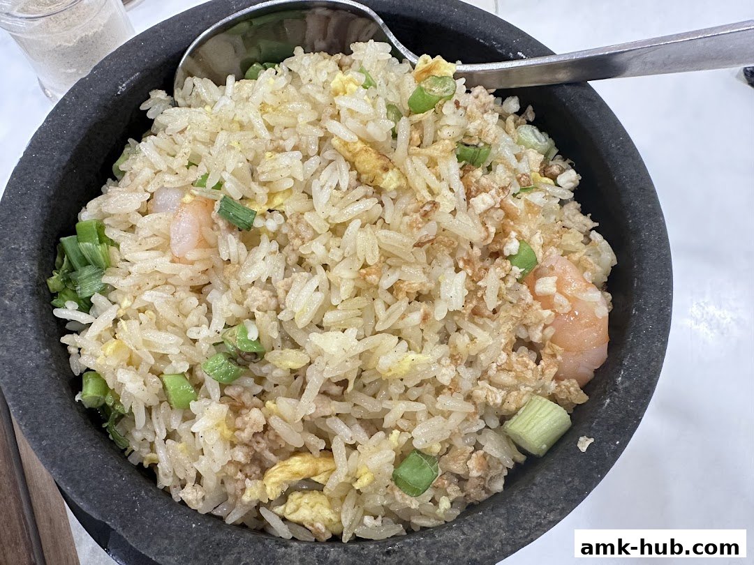 A close-up shot of a stone bowl filled with savory fried rice, featuring shrimp and green onions.