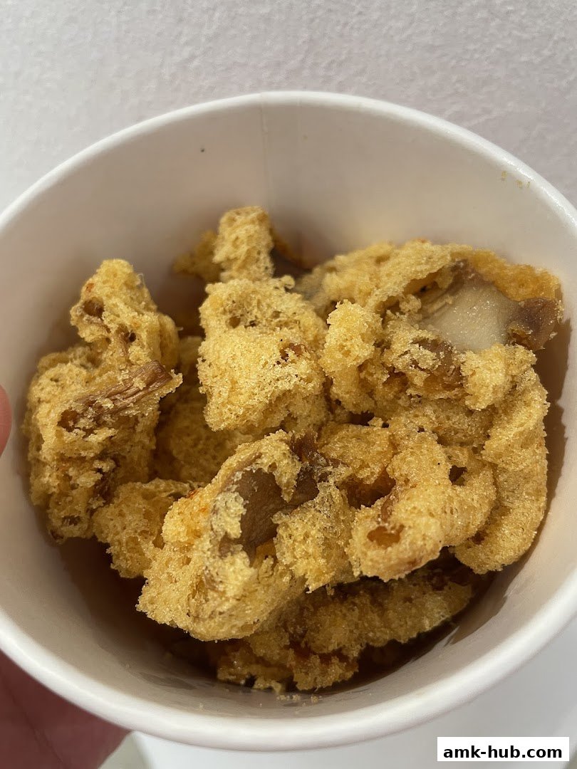 A close-up shot of crispy, golden-brown fried dough pieces in a white paper cup.