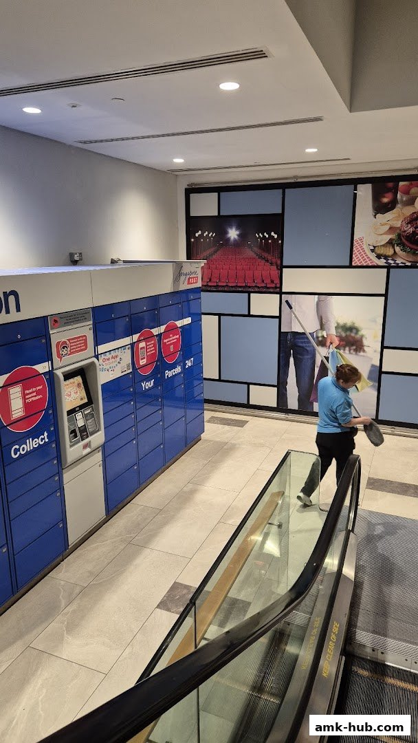 A POPStation parcel locker bank with a cleaner on an escalator in the background.