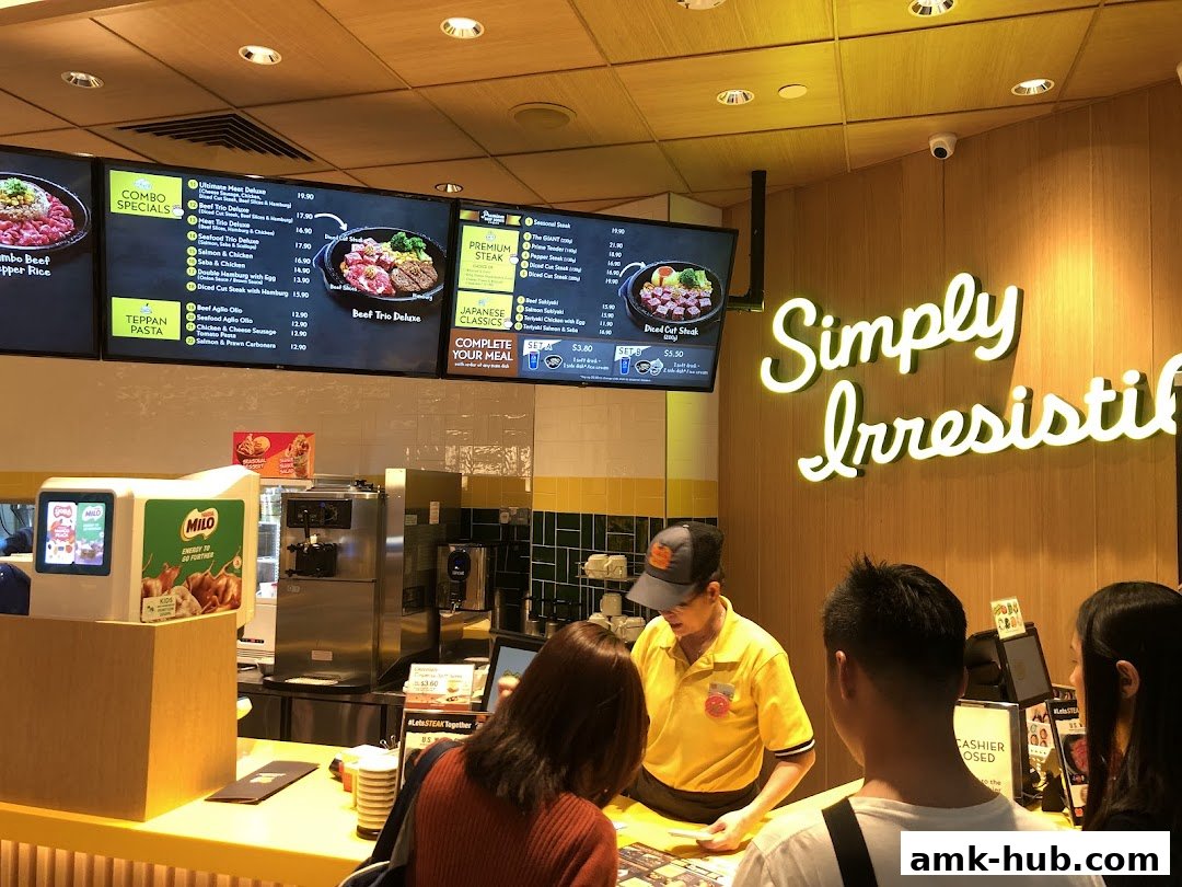 Customers ordering at a Pepper Lunch counter with menu screens and a neon sign.
