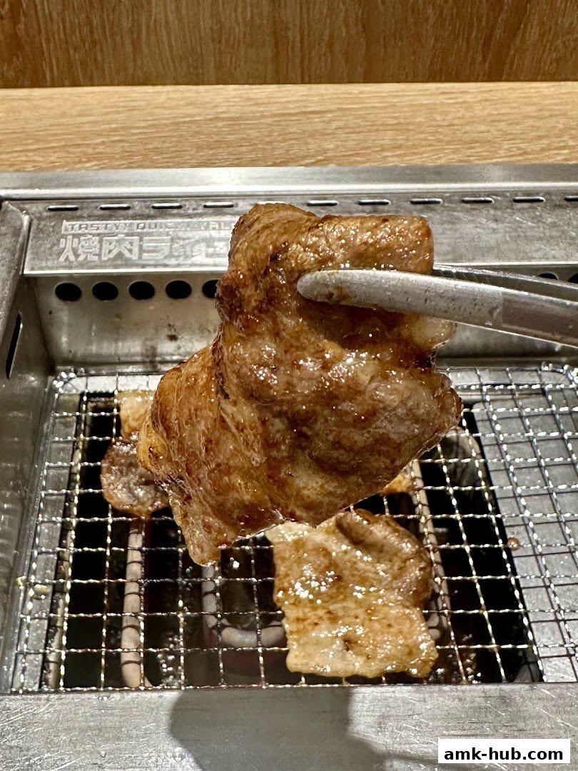 A piece of grilled meat is being held with tongs over a grill at Yakiniku Like.