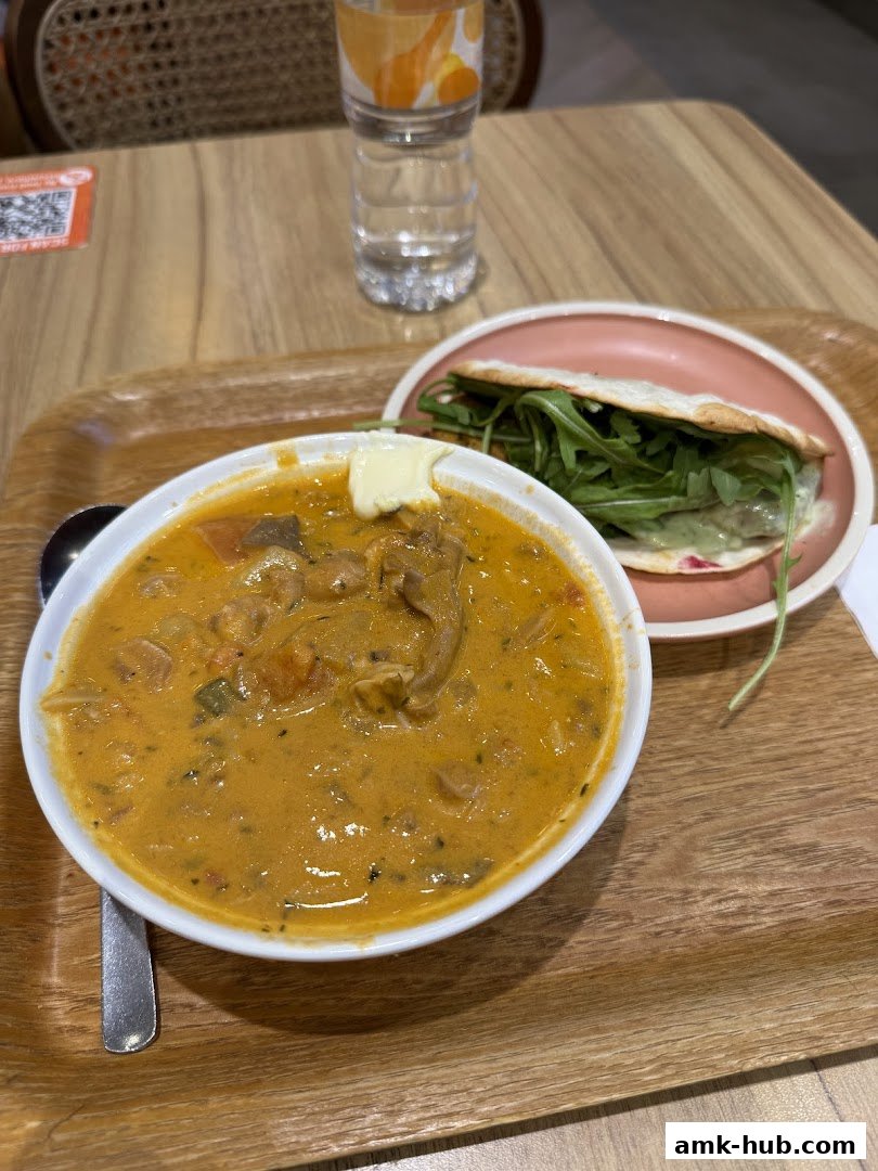 A bowl of creamy soup with a side of a wrap and a bottle of water.