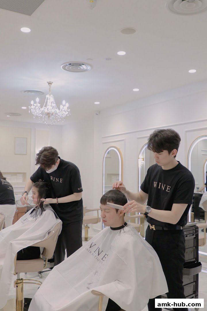 Stylists are cutting hair for clients in a bright, modern salon with a chandelier.