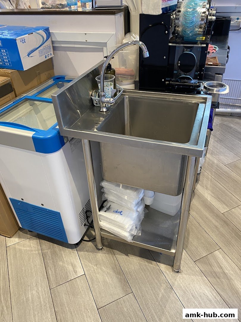A stainless steel sink with a faucet and various supplies next to a refrigerator.