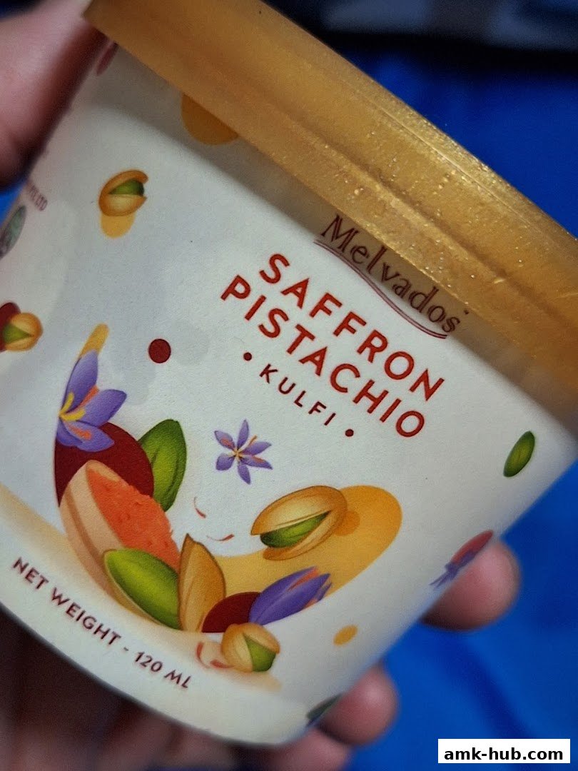 A hand holds a Melvados Saffron Pistachio Kulfi ice cream cup.