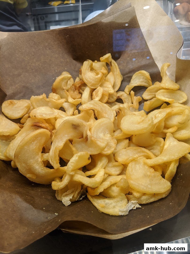 A close-up shot of freshly made, crispy potato chips served in a brown paper liner.