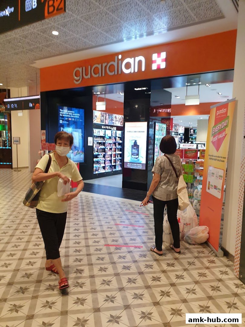 Two people stand in front of a Guardian Health & Beauty store with products displayed inside.