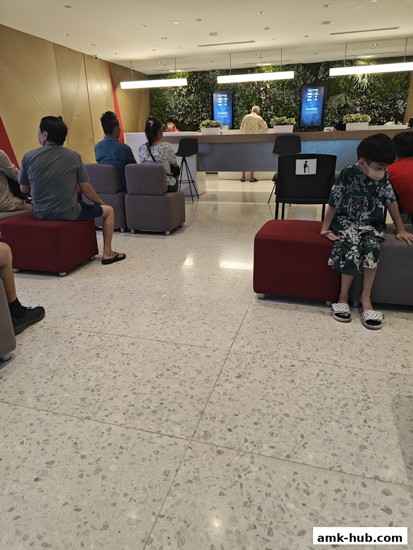 People waiting inside a modern bank with green wall decor and digital displays.