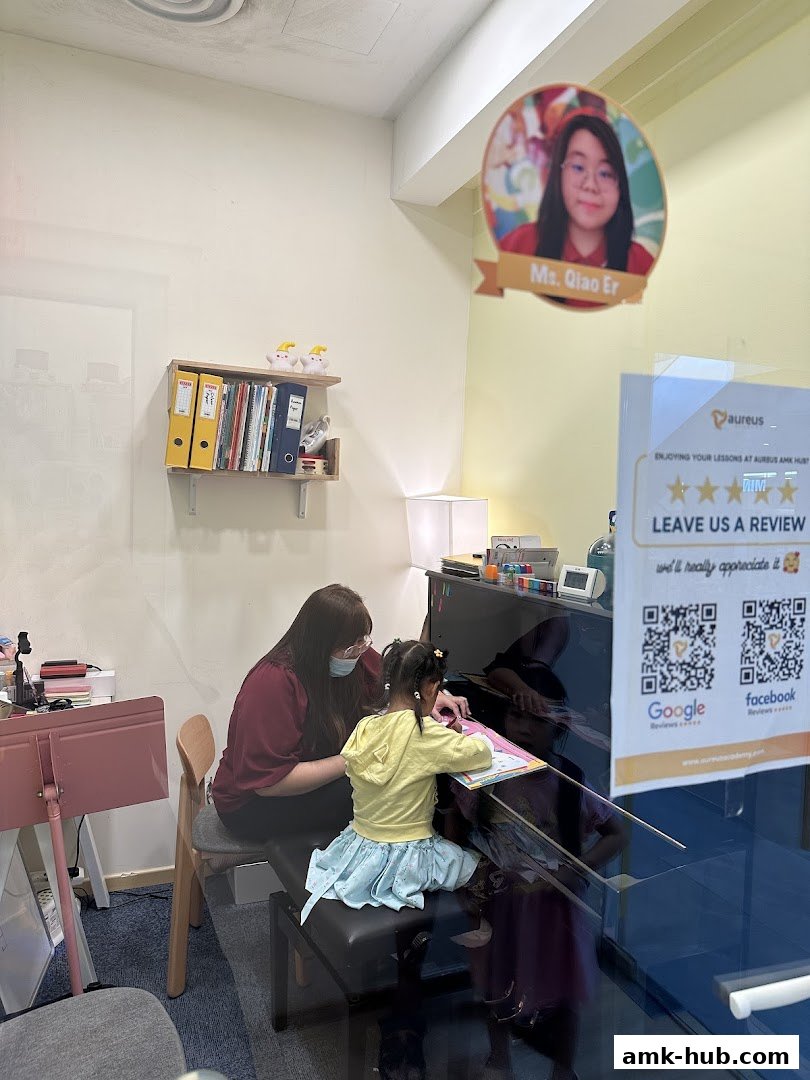 A teacher instructs a young student at a piano in a bright, modern classroom.